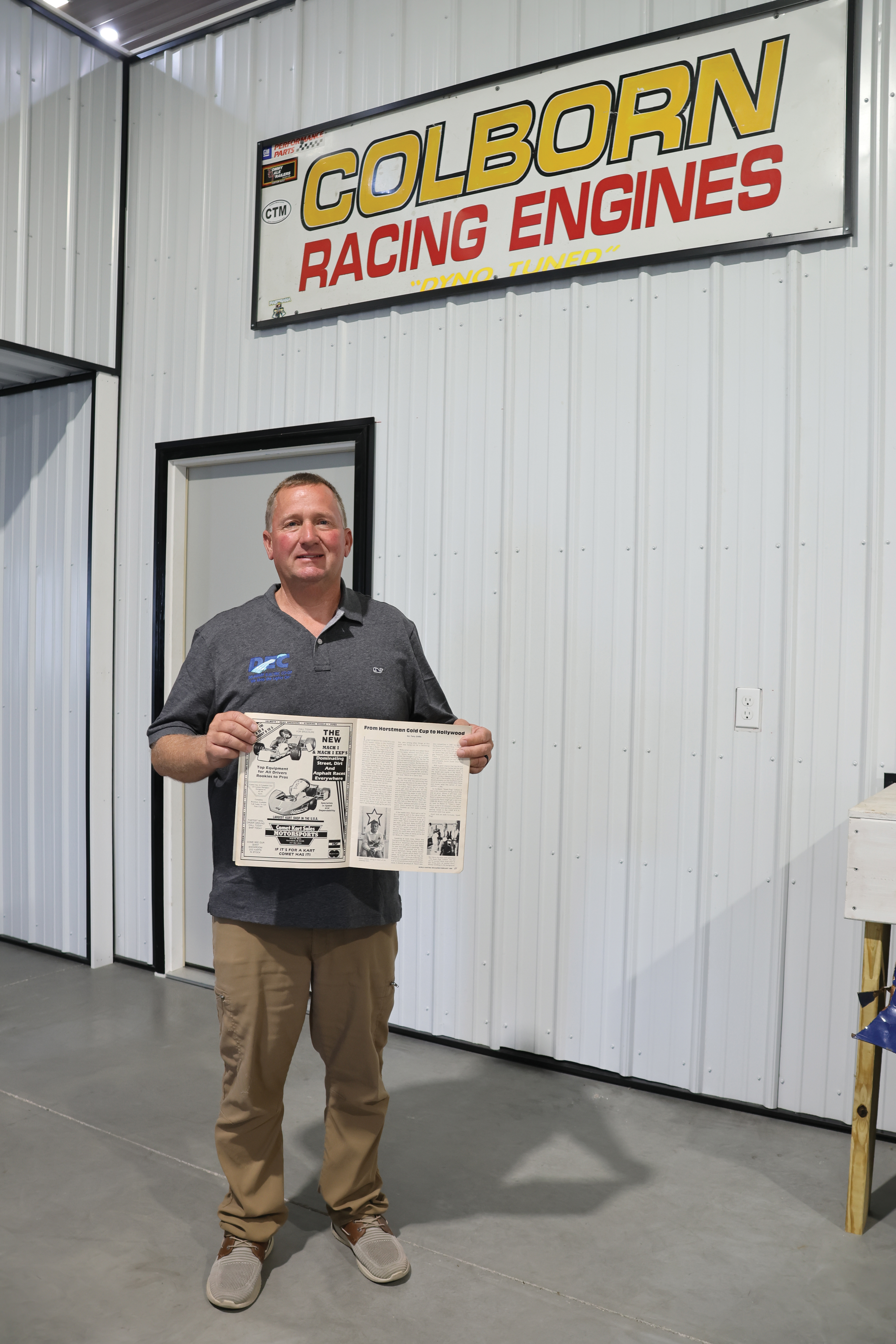 Colborn poses for a photo in his home shop, holding a copy of one of the World Karting Association magazines he was featured in as a teenager.
