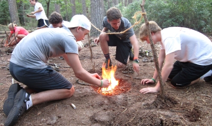 Boys kneeling around camp fire