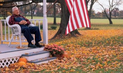 A man sits on his porch, enjoying a fall day.