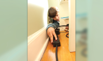 A boy attempts to turn off a power strip.