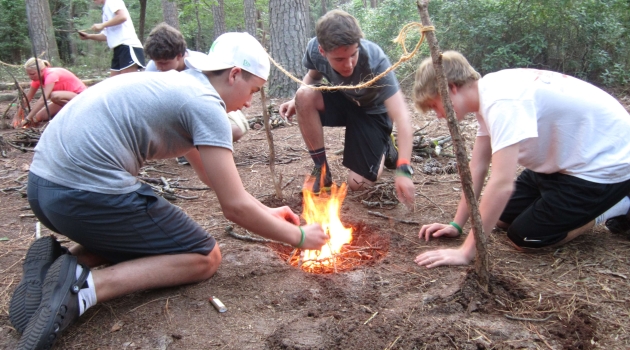 Boys kneeling around camp fire