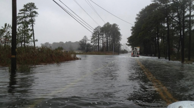 A DEC truck faces a roadway flooded by water following a major storm.