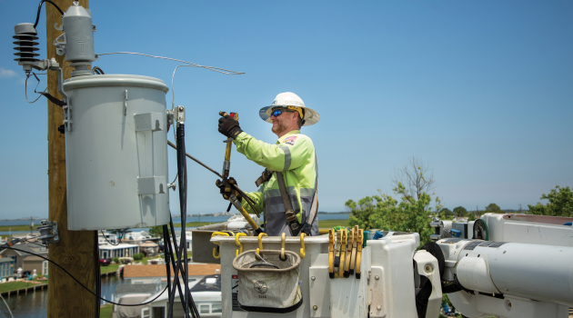 A DEC lineworker restores power using a bucket truck to reach a pole-top transformer.