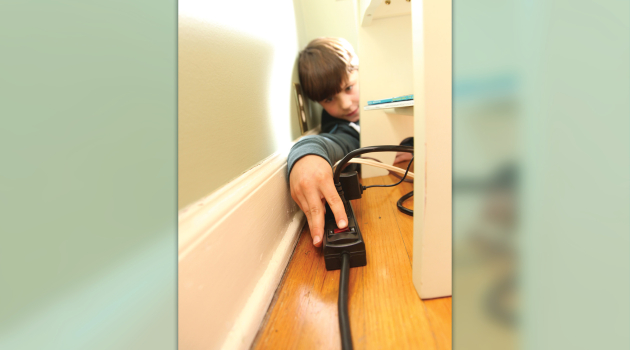 A boy attempts to turn off a power strip.